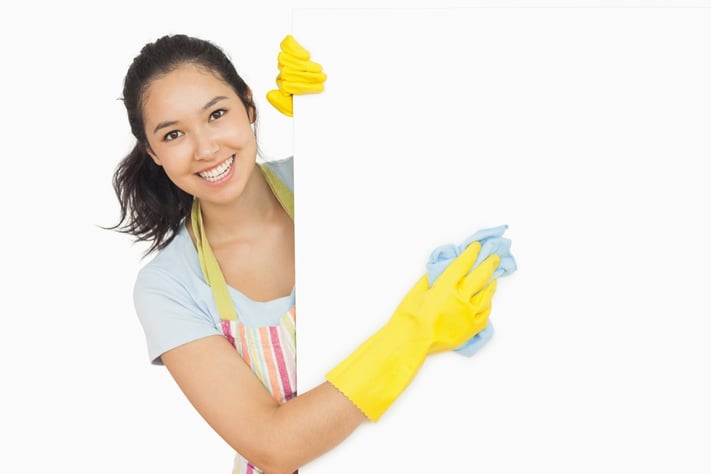 Cheerful woman cleaning white surface in apron and rubber gloves.jpeg
